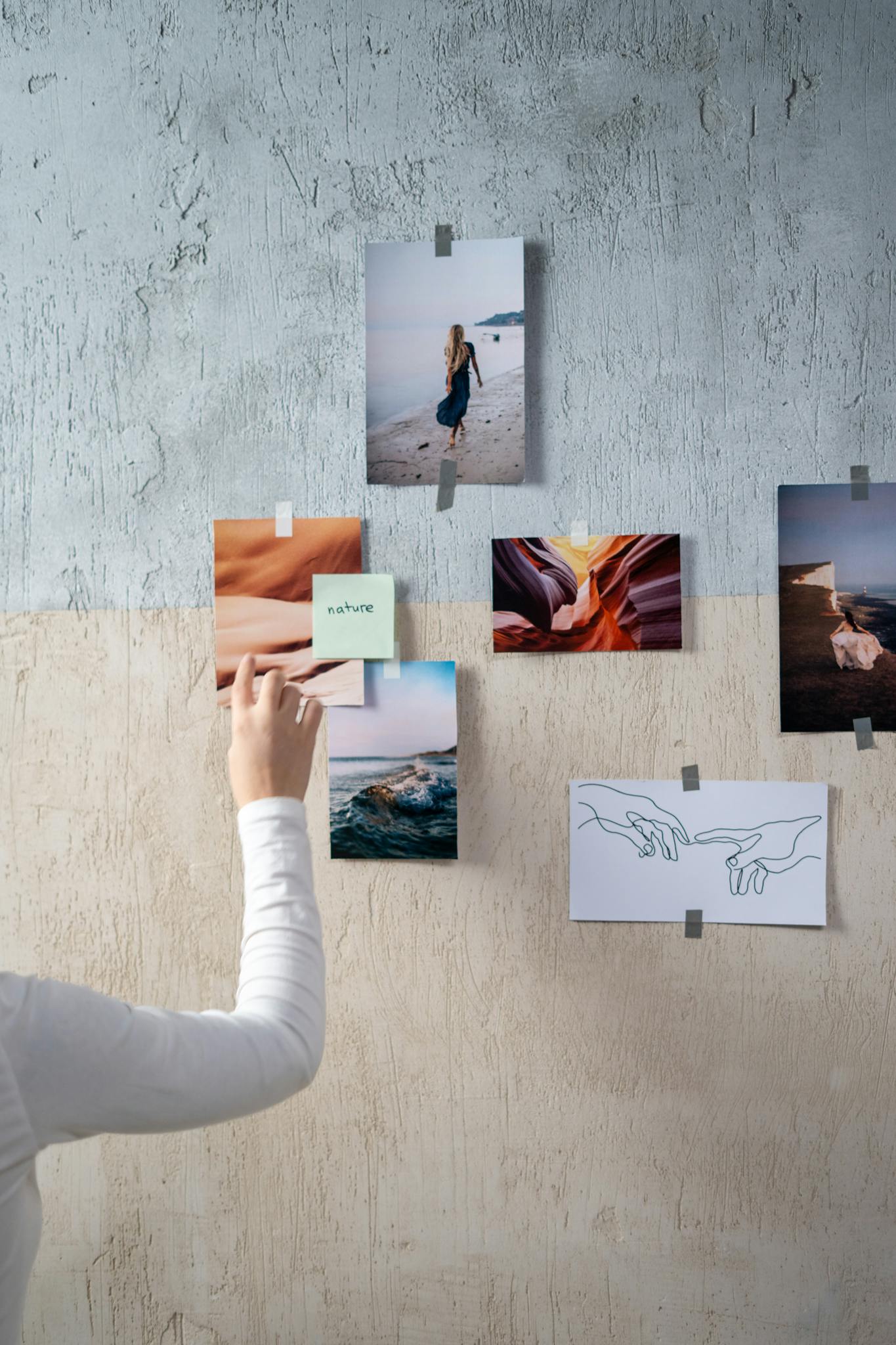 A person arranging various photographs on a textured wall.