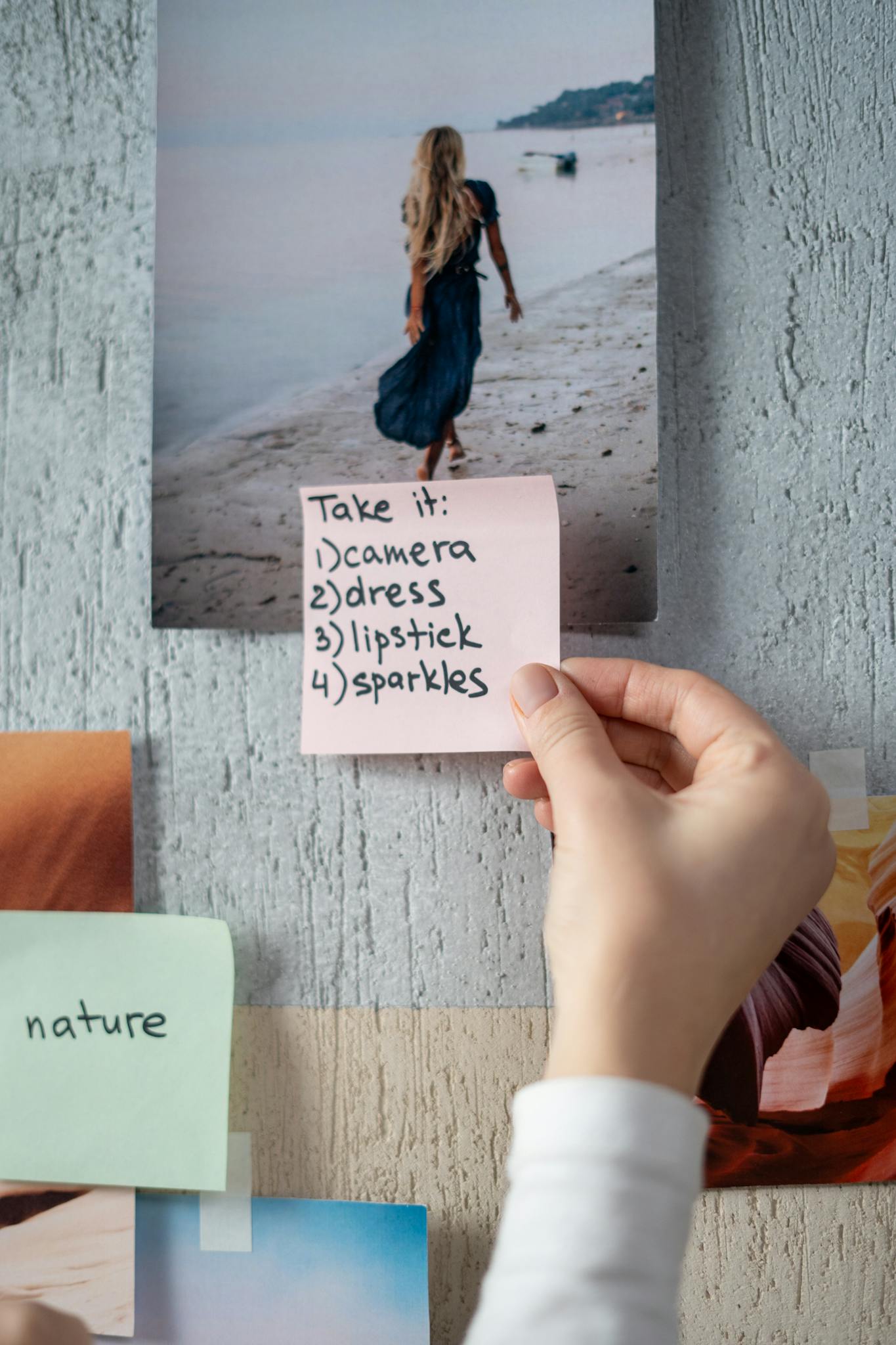 Hand holding a sticky note on a creative moodboard with a beach photo.